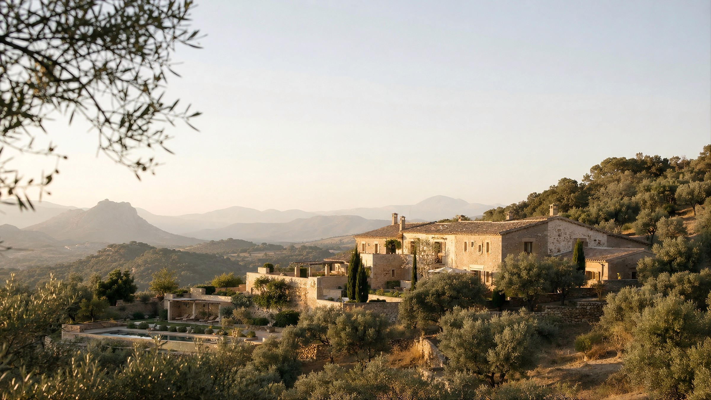 Panoramic golden-hour view of a sprawling stone villa estate in a mountainous landscape.