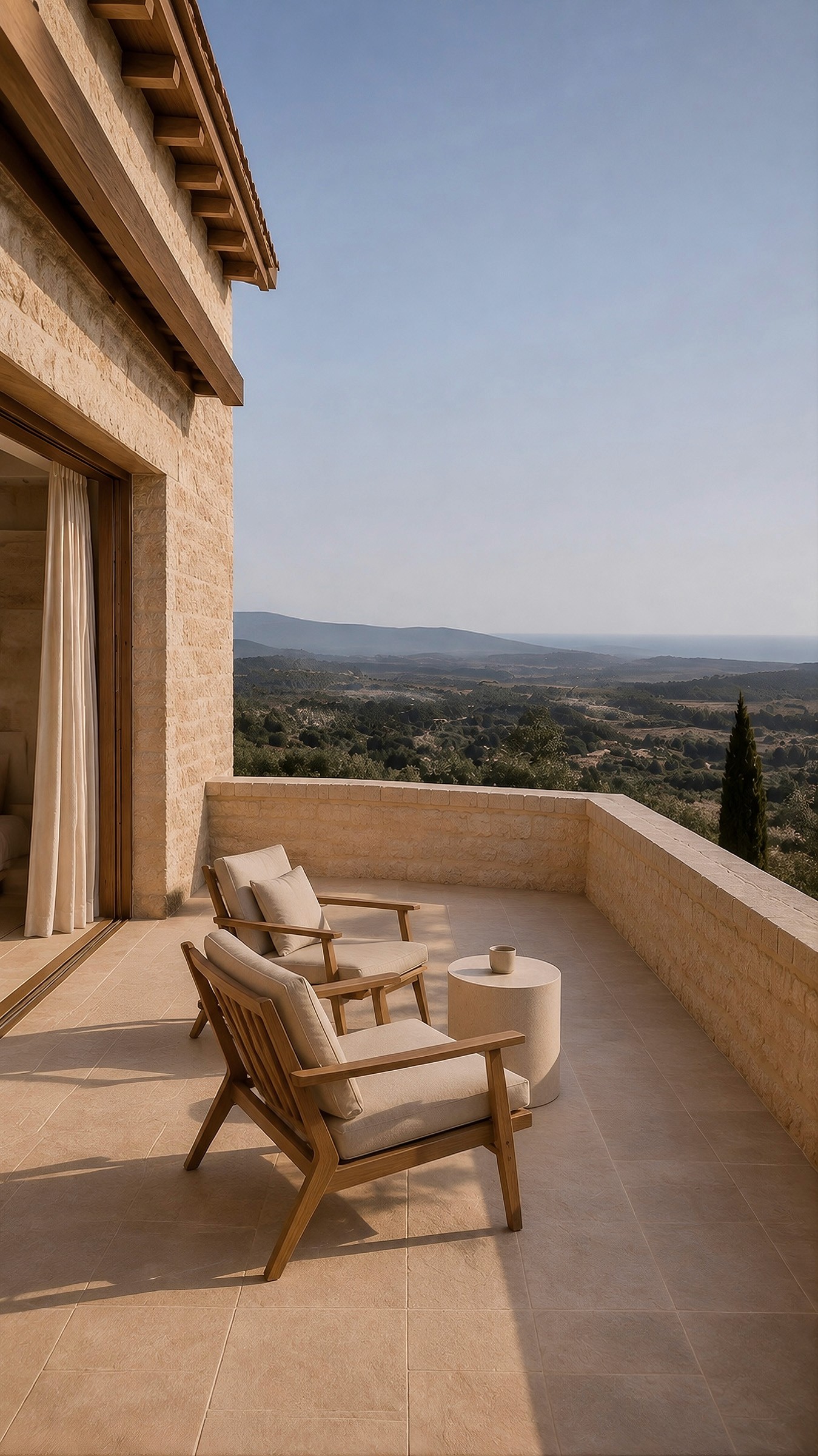 Stone terrace with two wooden lounge chairs overlooking a vast valley and distant sea.
